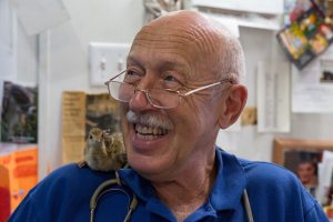Charles' peacock chick named Drogo perches on Dr. Pol's shoulder in the clinic. (Photo Credit: National Geographic Channels/Michael Stankevich)